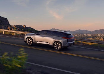 Silver SUV driving along a scenic mountain road at sunset with a city visible in the distance.